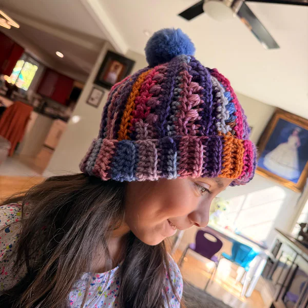 Young girl wearing a colorful ribbed crochet beanie with a pom-pom